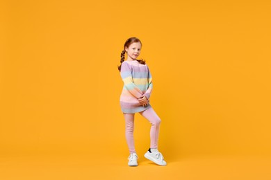 Photo of Cute little girl dancing on orange background