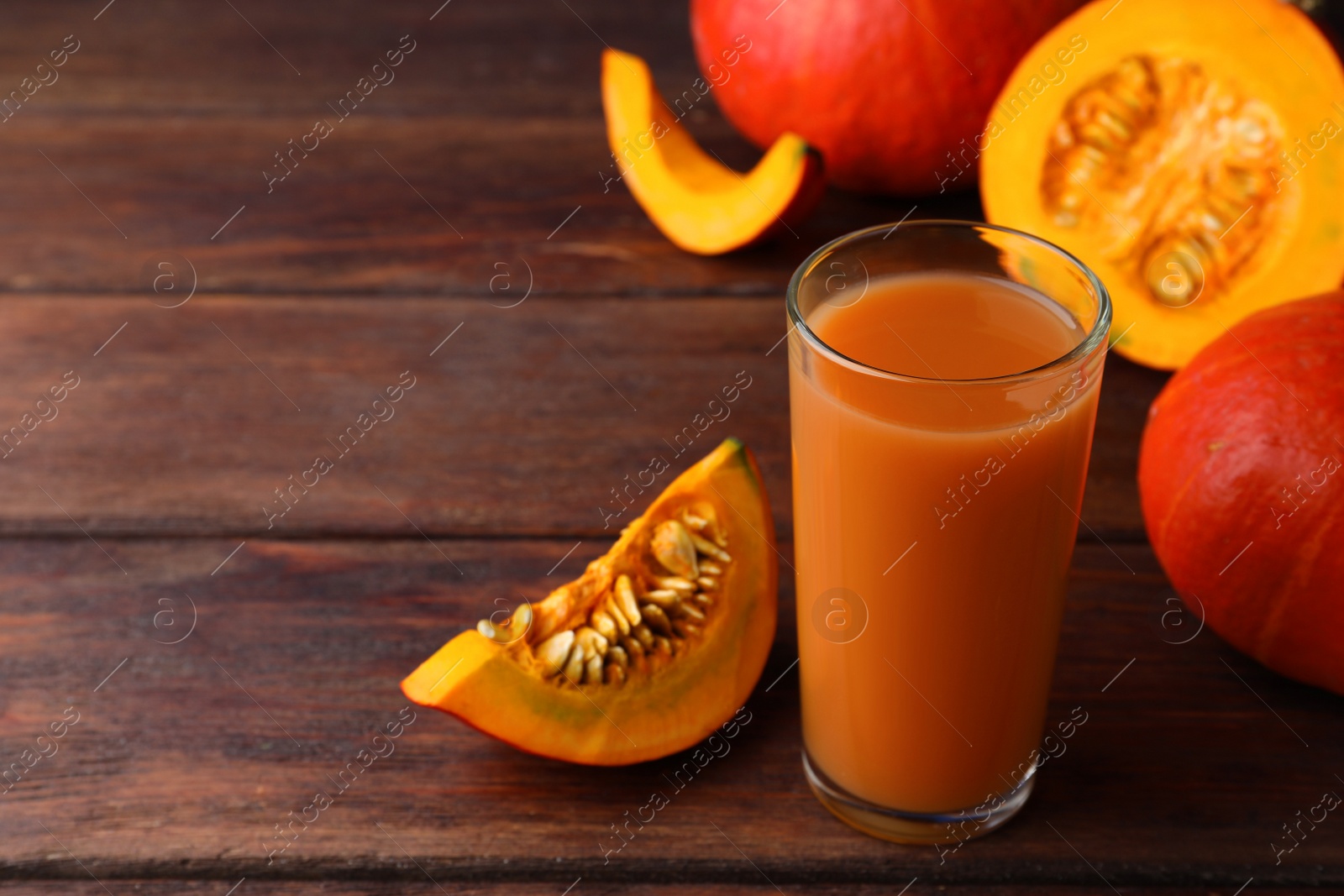 Photo of Tasty pumpkin juice in glass, whole and cut pumpkins on wooden table. Space for text