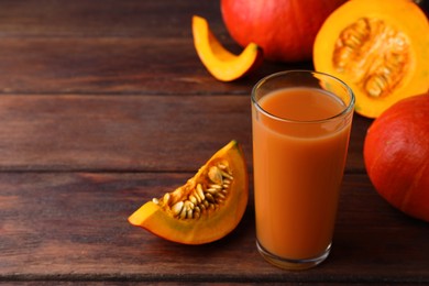 Photo of Tasty pumpkin juice in glass, whole and cut pumpkins on wooden table. Space for text