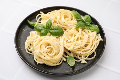 Photo of Delicious pasta with brie cheese and basil leaves on white tiled table, closeup