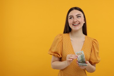 Photo of Happy woman with dollar banknotes on orange background, space for text