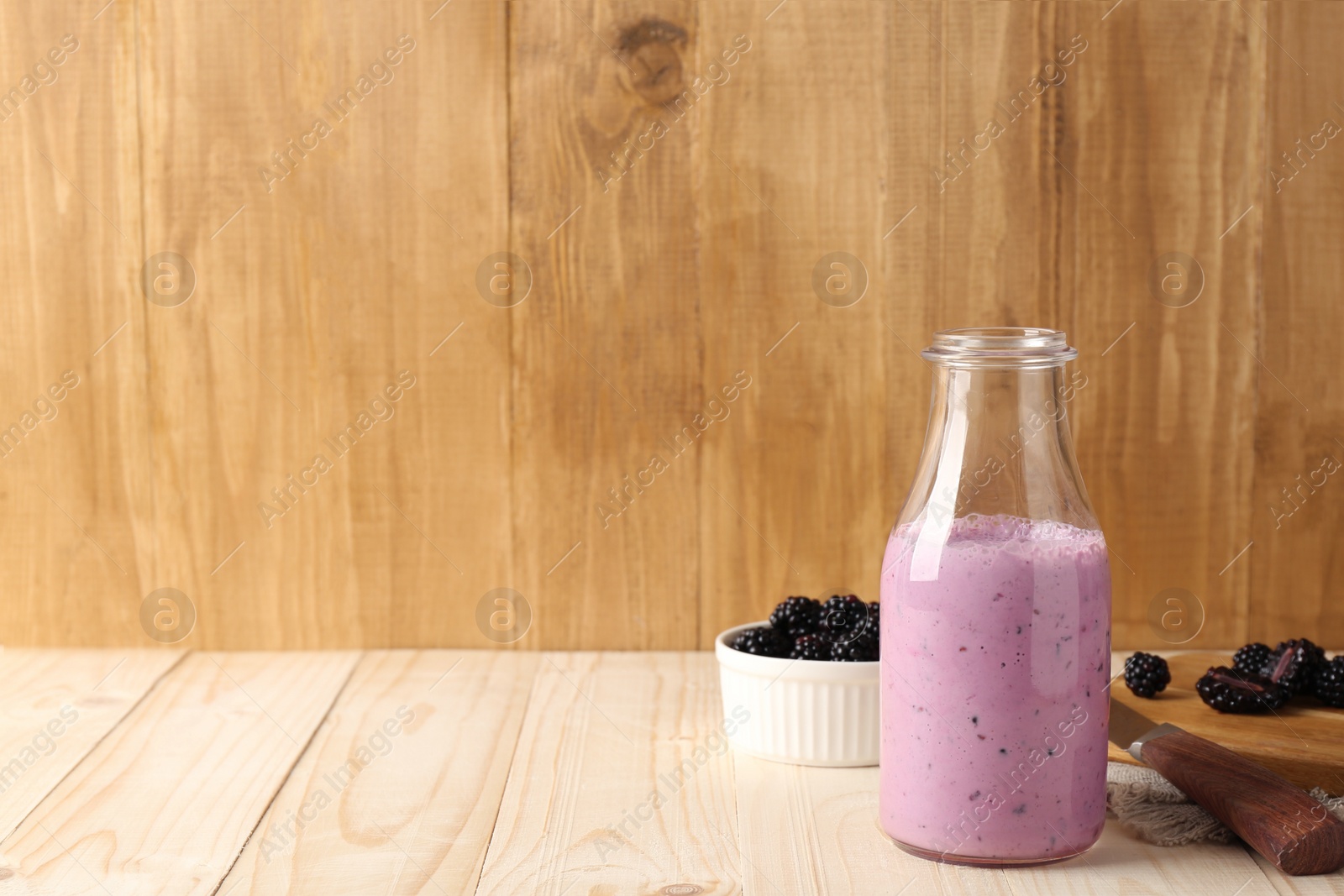 Photo of Delicious blackberry smoothie in glass bottle and fresh berries on wooden table. Space for text