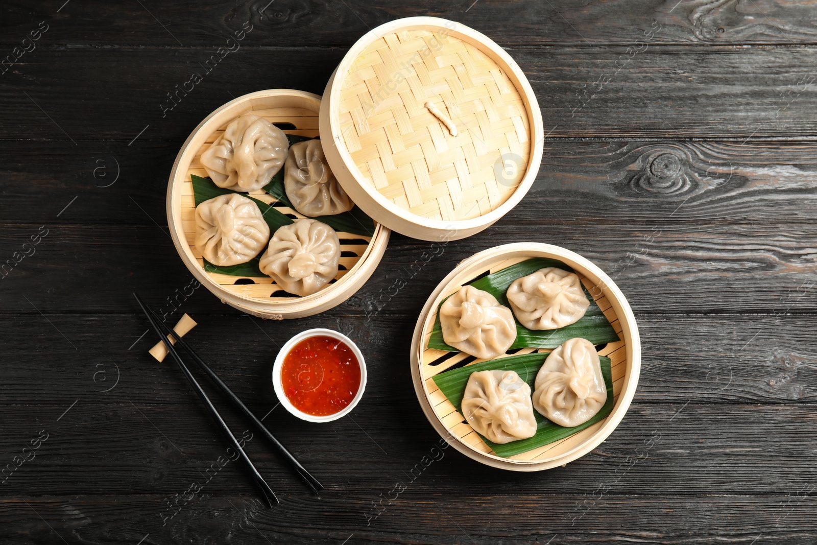 Photo of Bamboo steamers with tasty baozi dumplings, chopsticks and bowl of sauce on wooden background, top view