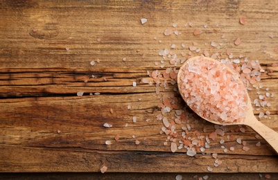 Photo of Spoon and pink himalayan salt on wooden table, flat lay. Space for text