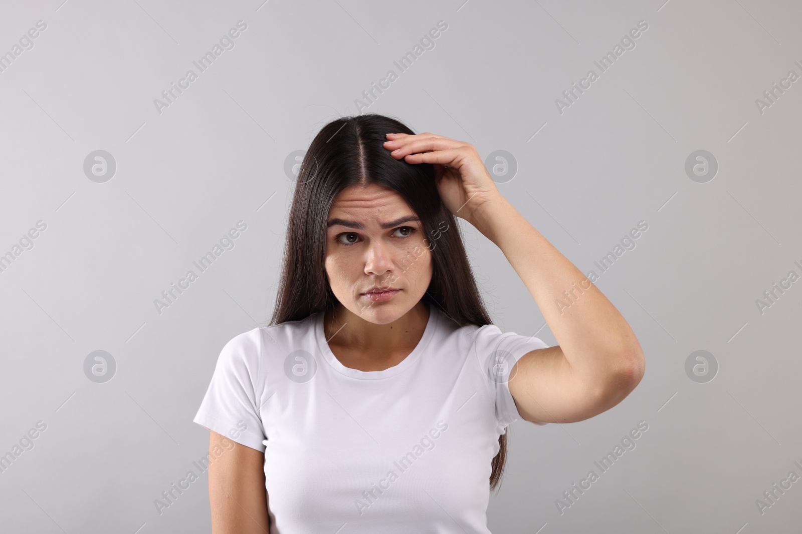 Photo of Emotional woman examining her hair and scalp on grey background