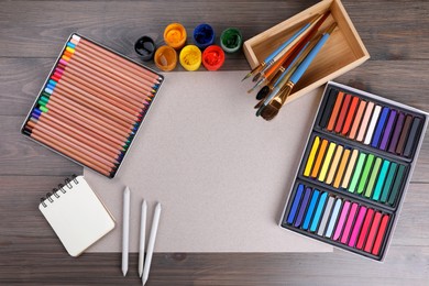 Blank sheet of paper, colorful chalk pastels and other drawing tools on wooden table, flat lay. Modern artist's workplace