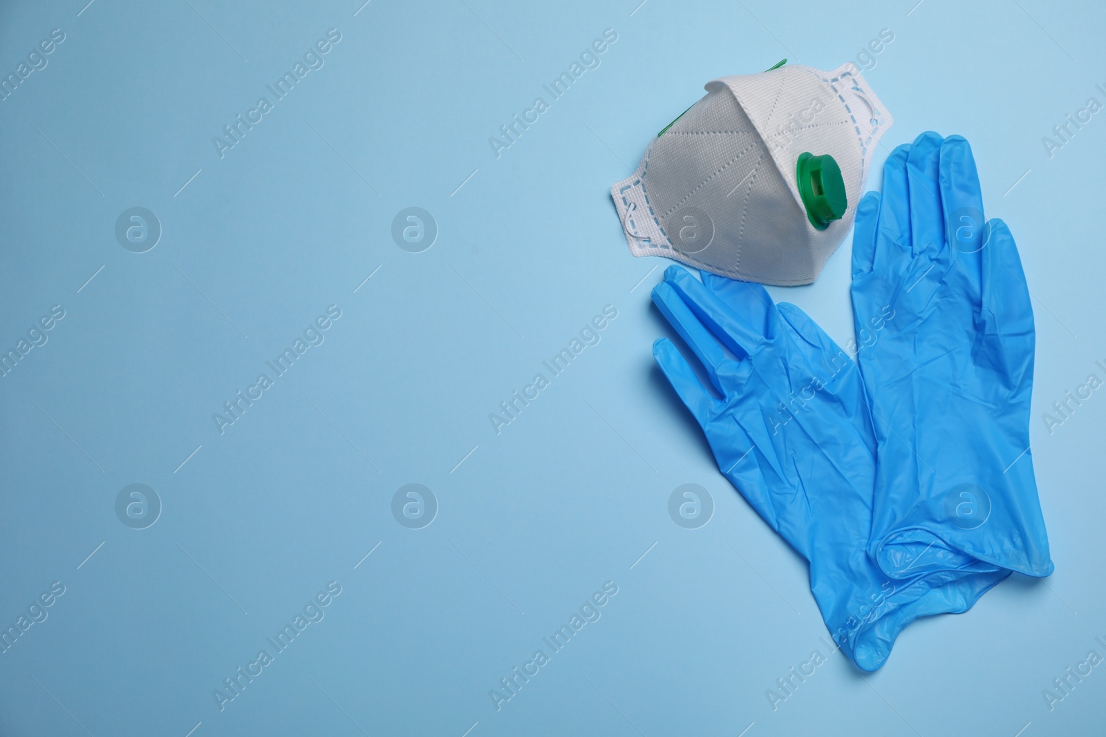 Photo of Medical gloves and respiratory mask on light blue background, flat lay with space for text. Safety equipment
