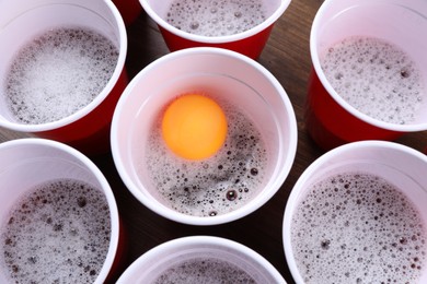 Plastic cups and ball for beer pong on wooden table, flat lay