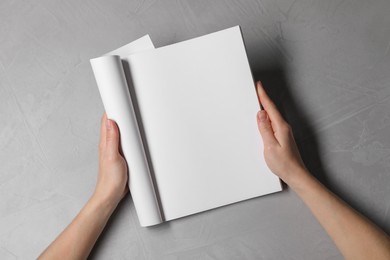 Photo of Woman holding notebook with blank pages at light grey table, top view. Mockup for design