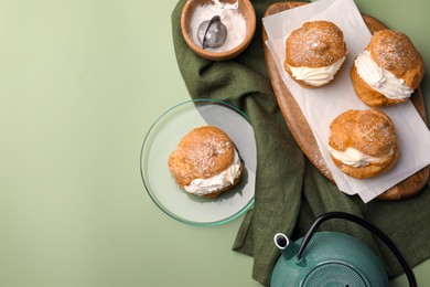Delicious profiteroles filled with cream and teapot on green background, flat lay. Space for text