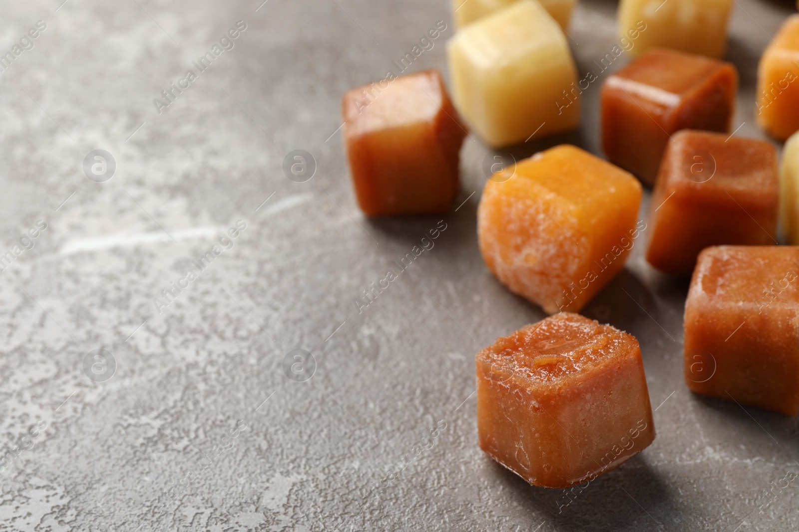 Photo of Different frozen fruit puree cubes on brown marble table, closeup. Space for text