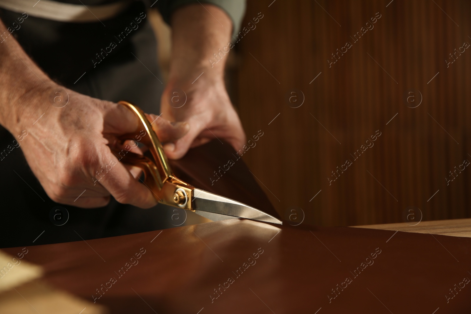 Photo of Man cutting leather with scissors in workshop, closeup