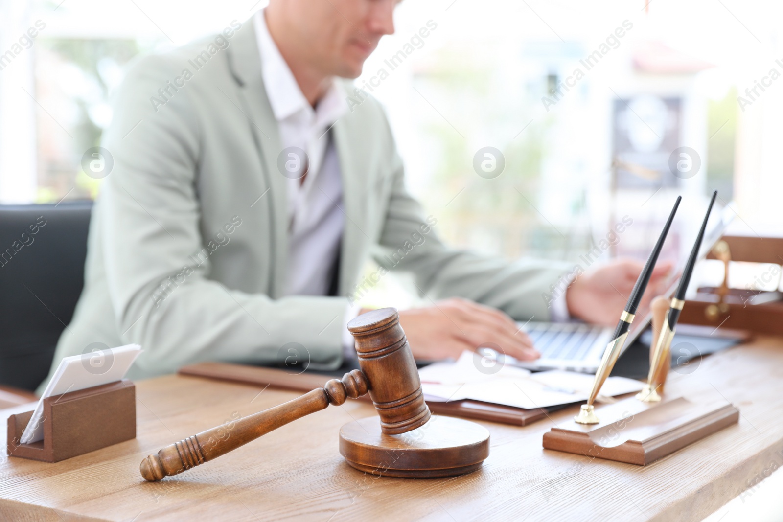 Photo of Wooden gavel and blurred notary with laptop on background