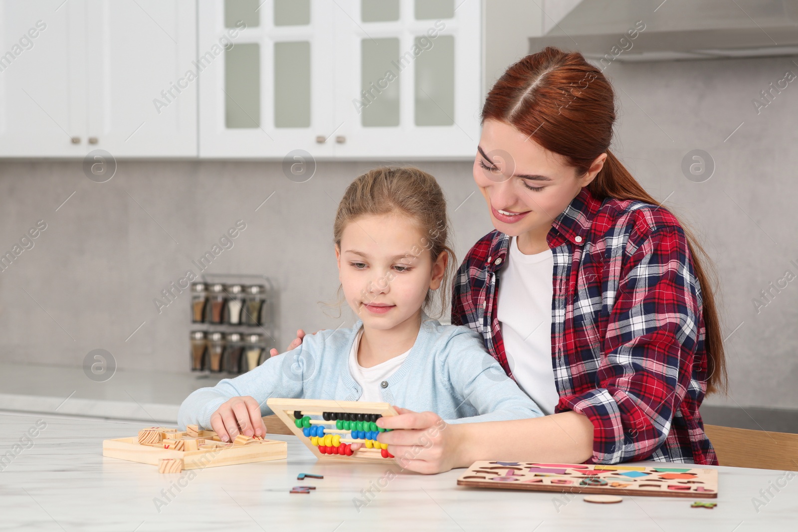 Photo of Happy mother and daughter playing with different math game kits at white marble table in kitchen. Study mathematics with pleasure