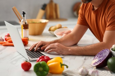 Man making dinner while watching online cooking course via laptop in kitchen, closeup