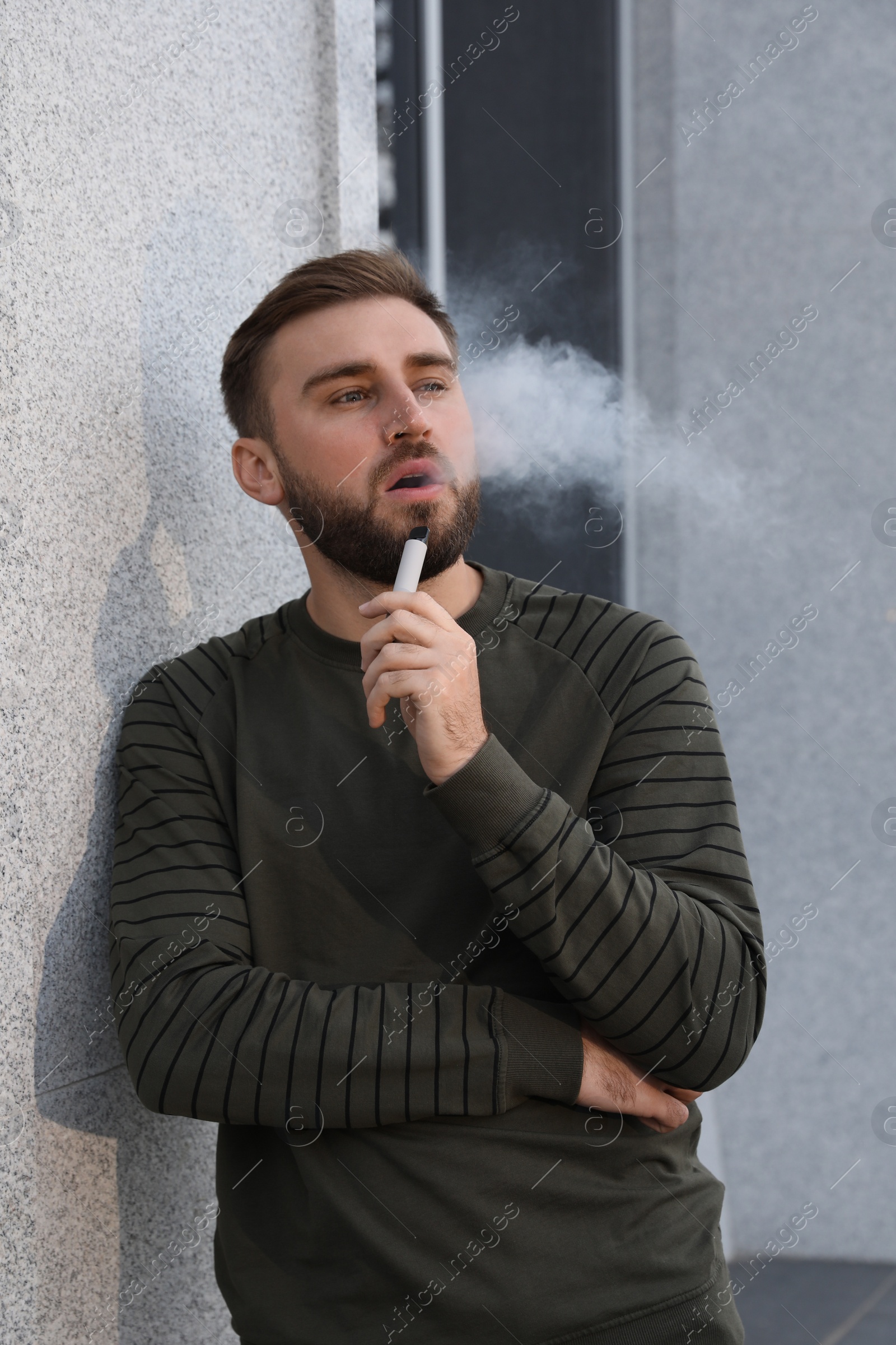 Photo of Handsome young man using disposable electronic cigarette outdoors