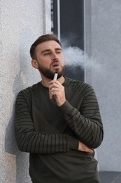 Photo of Handsome young man using disposable electronic cigarette outdoors