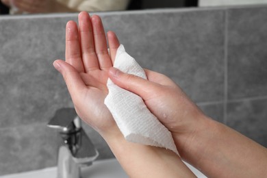 Woman wiping hands with paper towel in bathroom, closeup