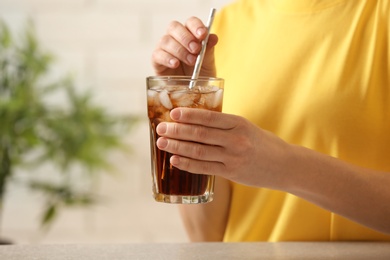 Woman holding glass of cola with ice at table, closeup. Space for text