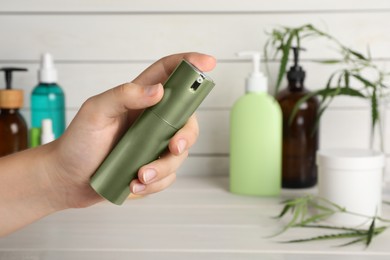 Photo of Woman holding bottle of cosmetic product with hemp extract over white wooden table, closeup