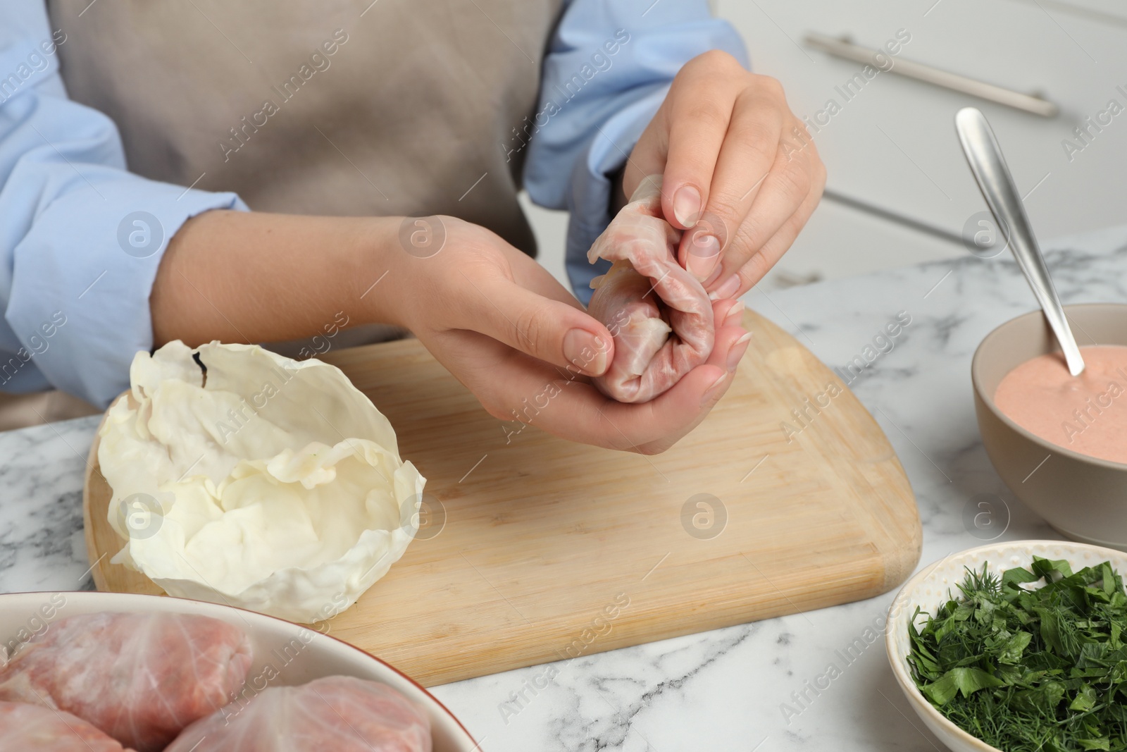 Photo of Woman making stuffed cabbage rolls at white marble table, closeup