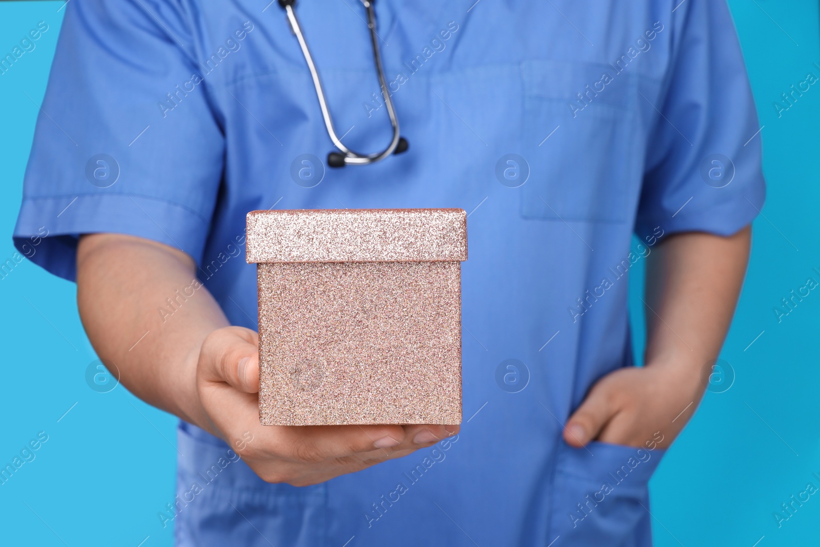 Photo of Doctor holding gift box on light blue background, closeup. Medical present