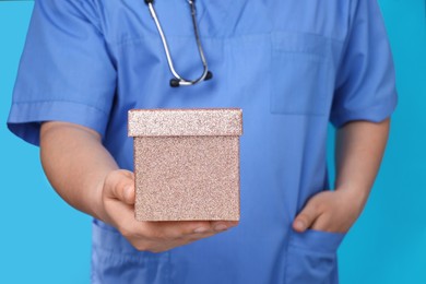 Photo of Doctor holding gift box on light blue background, closeup. Medical present