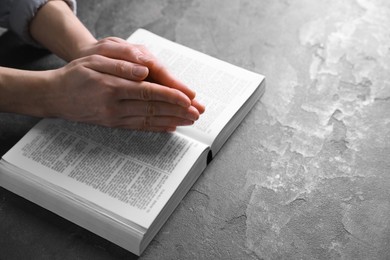 Photo of Religion. Christian woman praying over Bible at gray table, closeup. Space for text