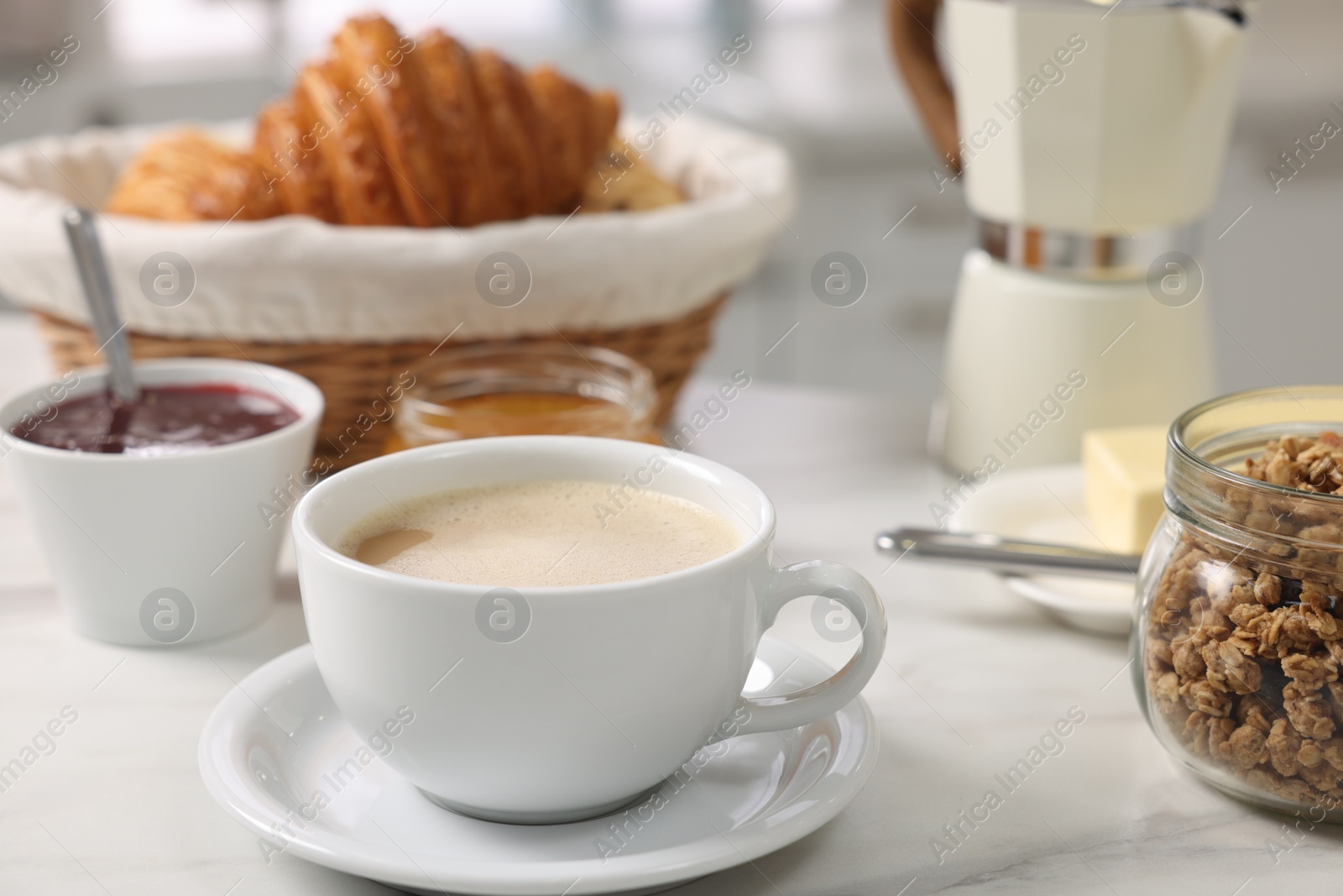 Photo of Breakfast time. Fresh coffee, granola, croissants, jam and honey on white table, closeup