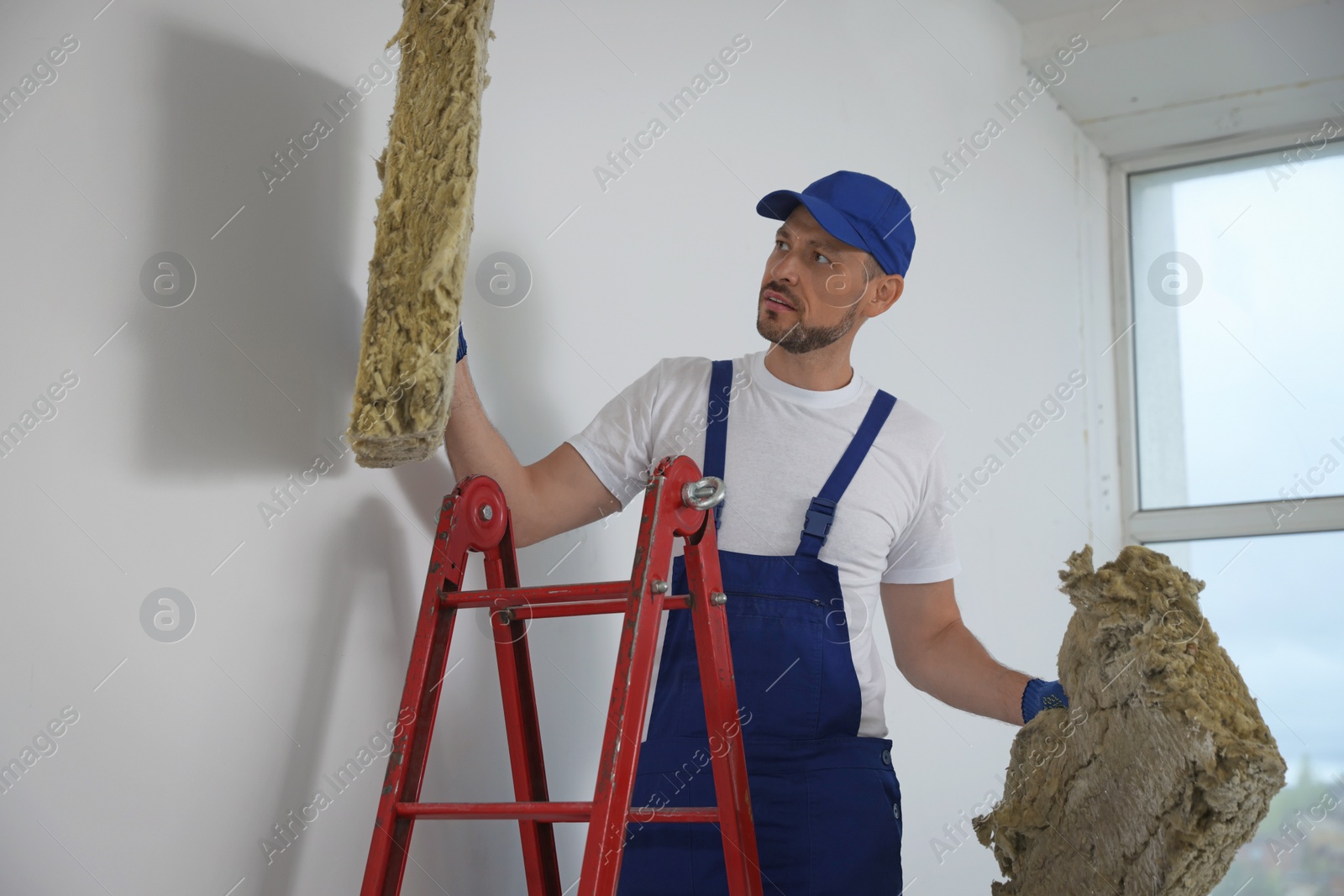 Photo of Construction worker with used glass wool on stepladder in room prepared for renovation