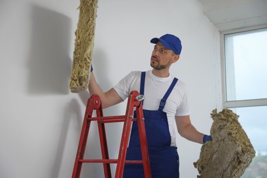 Construction worker with used glass wool on stepladder in room prepared for renovation