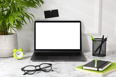 Photo of Office workplace with computer, glasses, houseplant and stationery on marble table near white wall