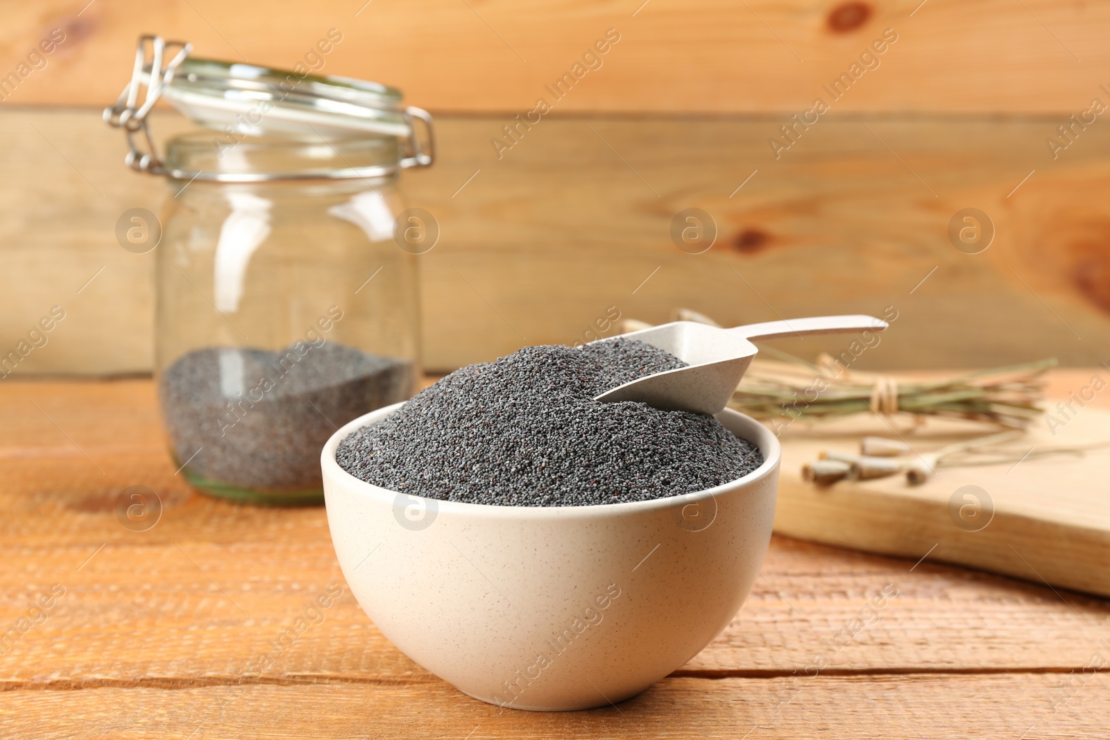 Photo of Poppy seeds and scoop in bowl on wooden table