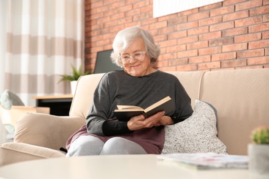 Photo of Elderly woman reading book on sofa in living room