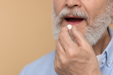 Photo of Senior man taking pill on beige background, closeup. Space for text