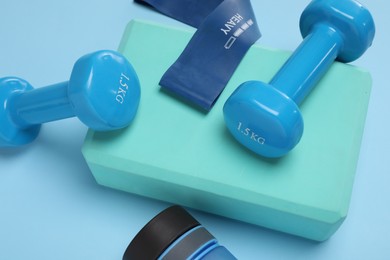 Photo of Two dumbbells, yoga block, fitness elastic band and bottle on light blue background, above view