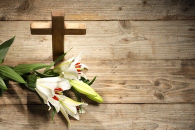 Photo of Cross and lilies on wooden background, above view with space for text. Religion of Christianity
