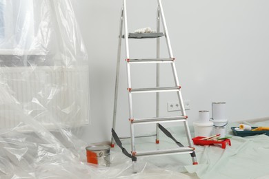 Photo of Metallic folding ladder and painting tools indoors