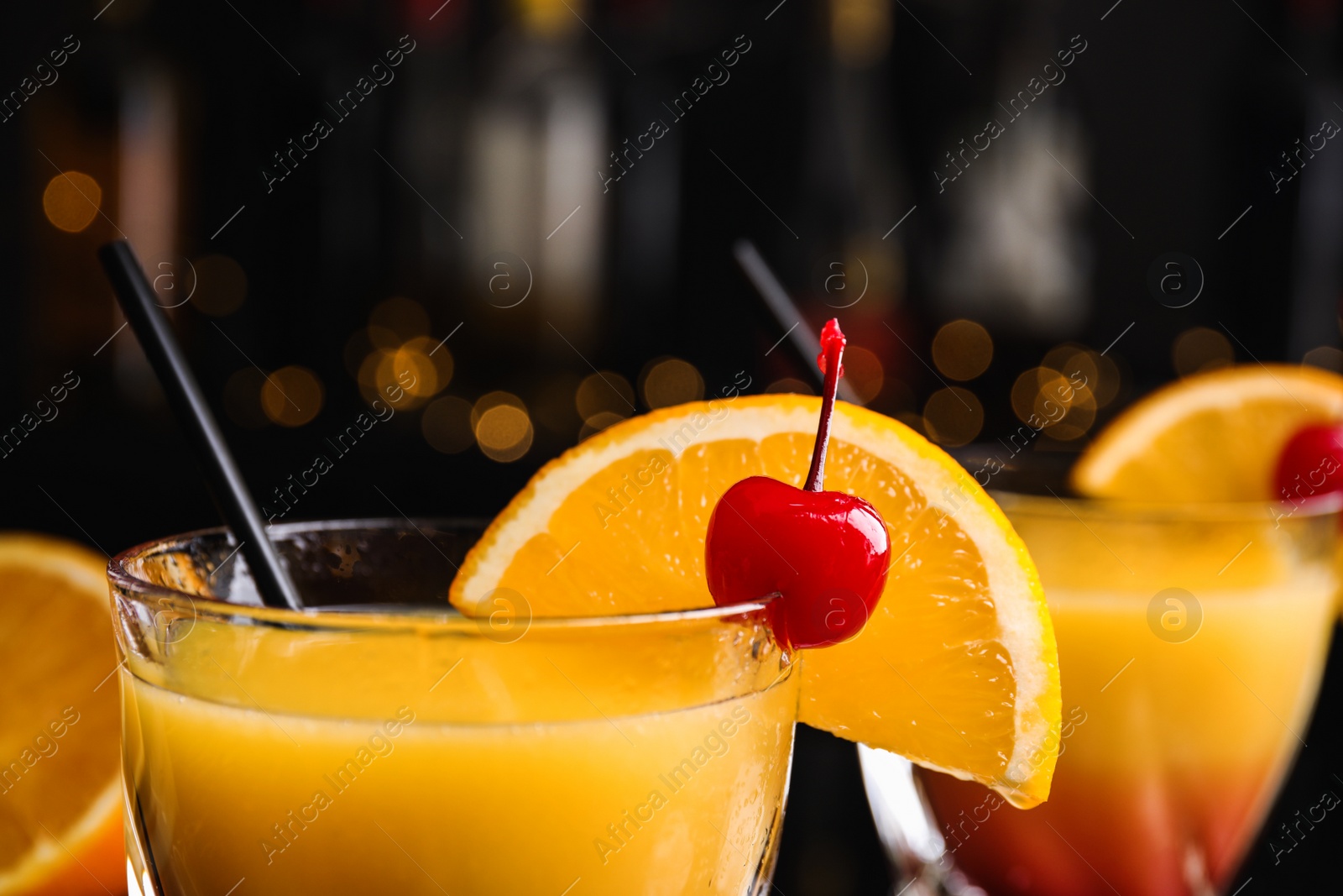 Photo of Fresh alcoholic Tequila Sunrise cocktail against blurred lights, closeup