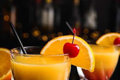 Photo of Fresh alcoholic Tequila Sunrise cocktail against blurred lights, closeup