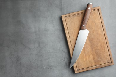 Photo of Knife and wooden board on grey textured table, top view. Space for text