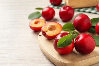 Delicious ripe cherry plums with leaves on white wooden table. Space for text