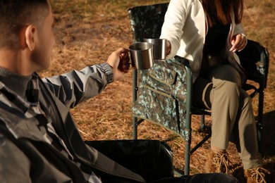 Couple resting in camping chairs and enjoying hot drink outdoors, closeup