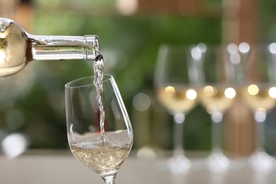 Photo of Pouring white wine from bottle into glass on blurred background, closeup. Space for text