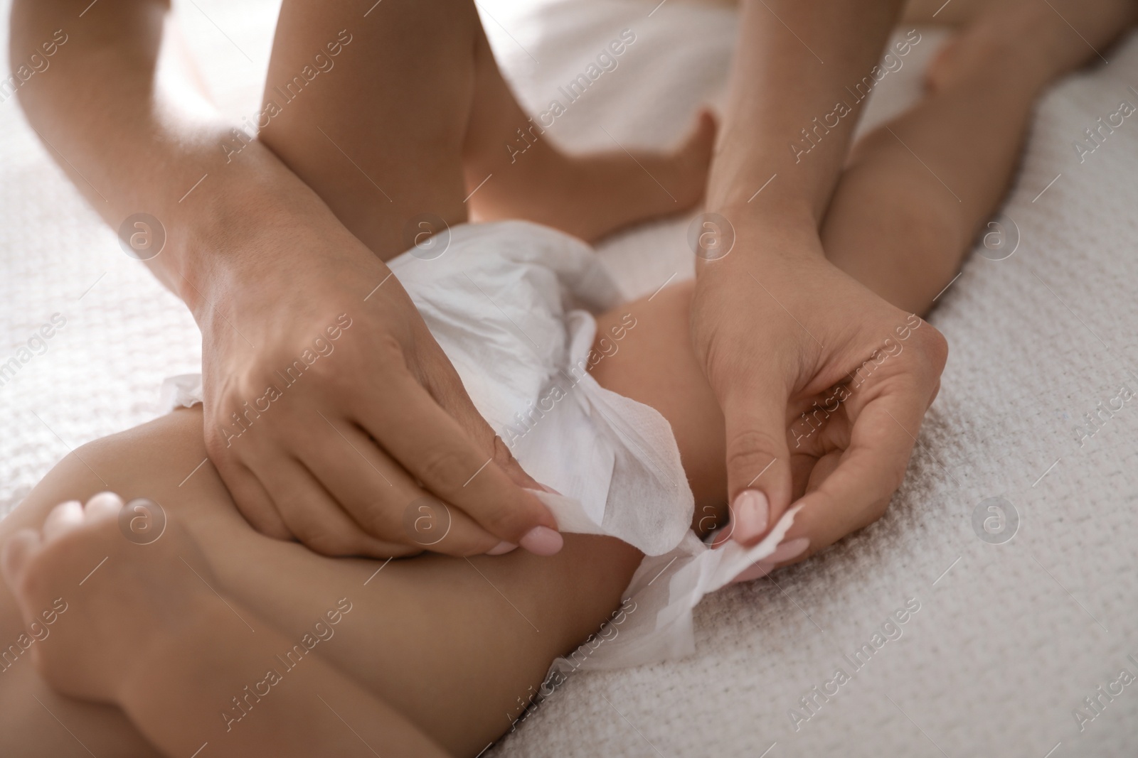 Photo of Mother changing baby's diaper on bed at home, closeup