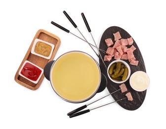 Photo of Oil in fondue pot, forks, pickles, sauces and pieces of raw meat isolated on white, top view