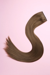 Photo of Lock of brown straight hair on color background, top view