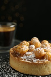 Photo of Delicious tart with hazelnuts, sweet caramel and powdered sugar on black table, closeup