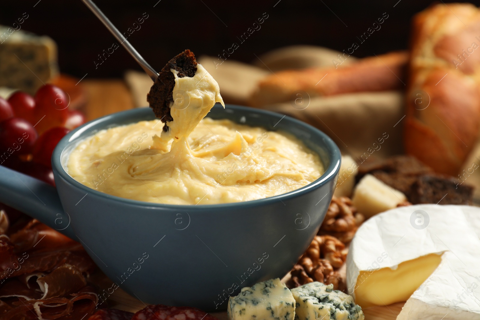 Photo of Dipping piece of bread into fondue pot with melted cheese at table, closeup