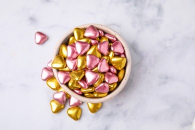 Bowl and delicious heart shaped candies on white marble table, flat lay